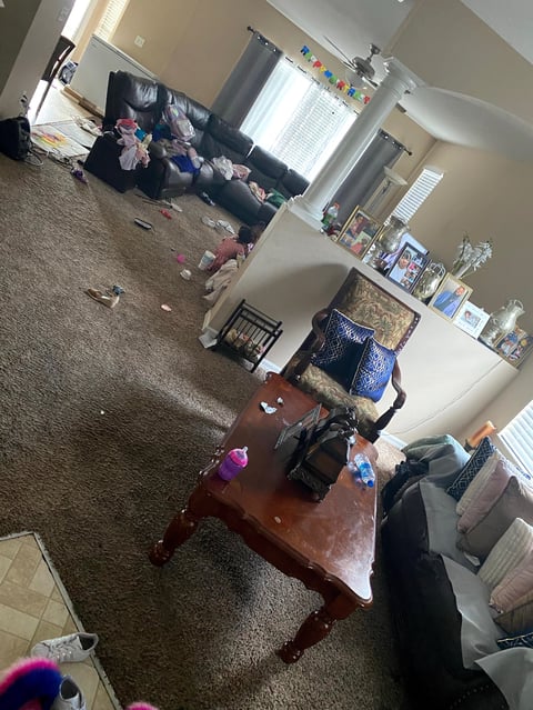 Overhead view of a cluttered bedroom with clothes scattered on floor, unmade bed with black comforter, desk, and storage items