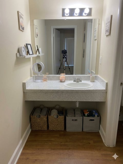 Modern bathroom vanity with white quartz countertop, integrated sink, lit mirror, and storage baskets underneath