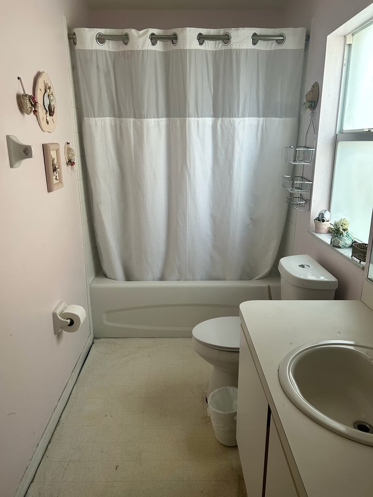 Small bathroom with gray shower curtain, toilet, sink, and window with natural light