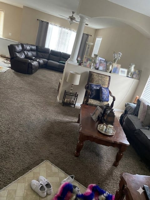 Spacious living room with black leather sectional sofa, wood table, beige carpet, and ceiling fan with bright windows